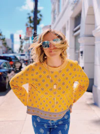a woman in a yellow sweater and jeans standing on a sidewalk